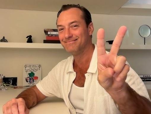 Jude Law na planie filmowym, w dynamicznej pozie, w kostiumie postaci, z elementami scenografii w tle.