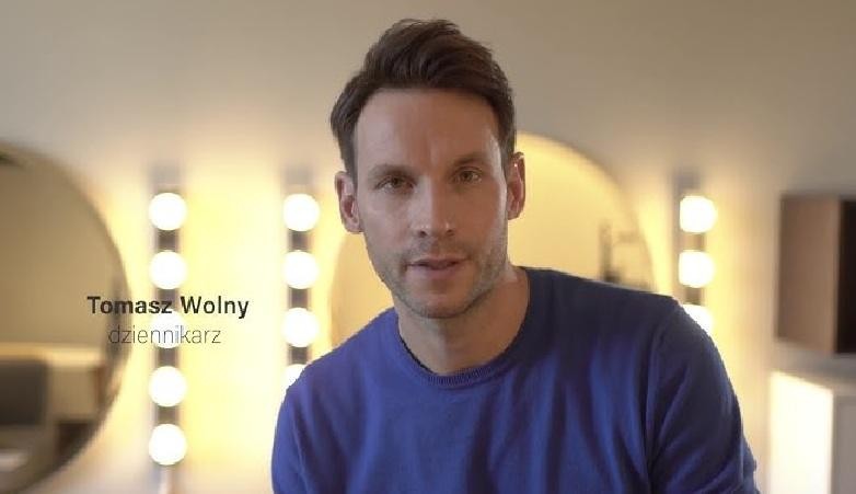 Tomasz Wolny z telefonem w ręku, uśmiechnięty, w tle subtelne nawiązania do jego pasji sportowych i akademickich, symbolizujące aktywność na Instagramie.