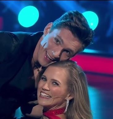 Agnieszka Kaczorowska w stroju tanecznym, wykonująca ruch taneczny w profesjonalnym studiu, symbolizująca jej rolę trenerki i pasję do tańca.