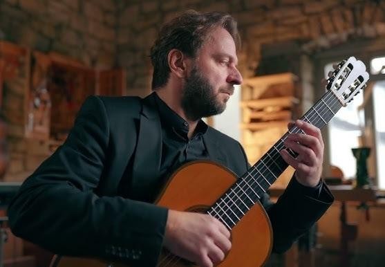 Marcin Dylla grający na gitarze klasycznej na scenie, oddający się muzyce, z rozmytym tłem sceny.