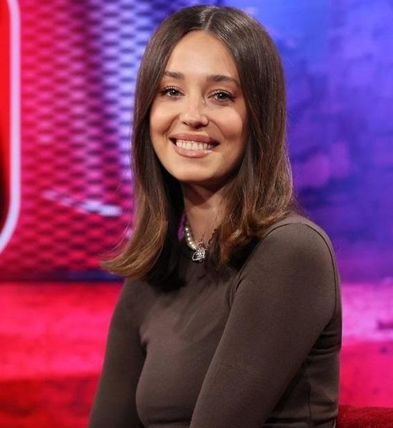 Izabella Krzan dynamicznie gestykulująca w studiu telewizyjnym, w kolorowym stroju, z uśmiechem prezentująca program.