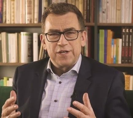 Maciej Orłoś podczas wystąpienia publicznego, gestykulujący w kierunku widza.