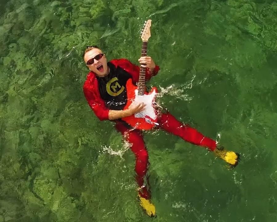 Alt: Czadoman (Paweł Dudek) podczas energicznego występu na scenie, śpiewający do mikrofonu, z dynamicznym oświetleniem i widownią w tle.
