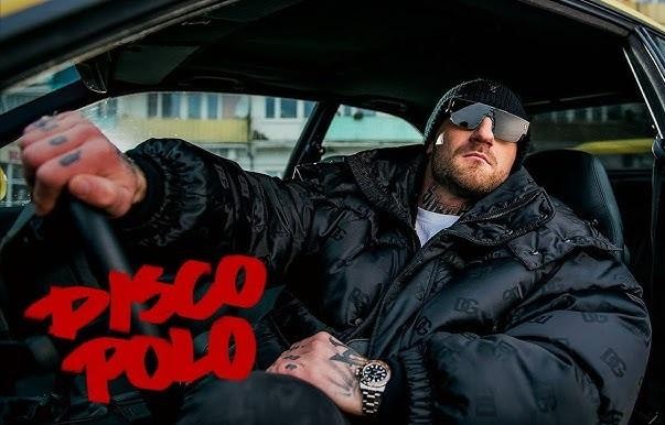 Kizo (Patryk Woziński) podczas energetycznego występu na scenie, trzymający mikrofon, z dynamicznym oświetleniem koncertowym.